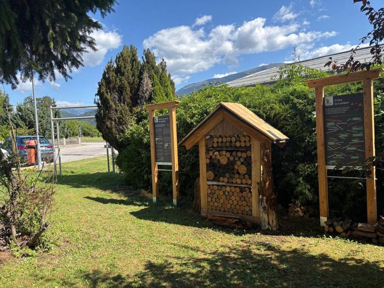 Insektenhotel und Info-Tafeln am Rand des Lehrpfads, im Hintergrund die Berge des Drautals