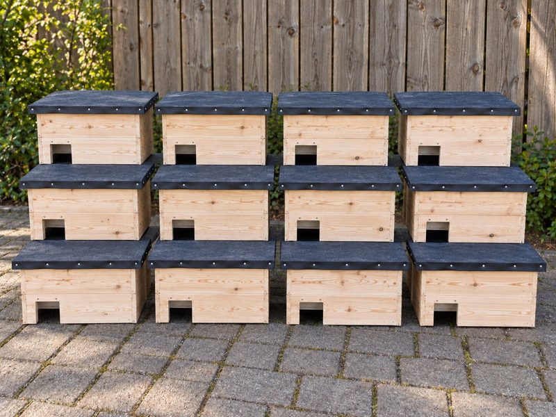 Zwölf fertige Igel-Schlafhäuser aus unbemaltem Naturholz mit schwarzer Dachpappe, gestapelt im Garten